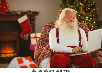 Santa claus typing on laptop at home in the living room - Powered by Shutterstock