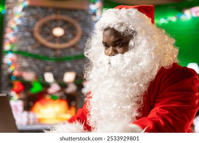 Santa Claus uses a laptop in his festive log cabin navigating online webpages to track gifts. The North Pole is filled with Christmas magic as Saint Nicholas embraces the digital age.