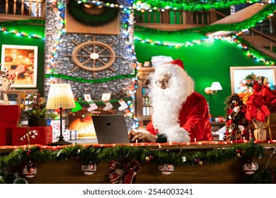 Santa Claus uses a laptop in his festive log cabin navigating online webpages to track gifts. The North Pole is filled with Christmas magic as Saint Nicholas embraces the digital age.