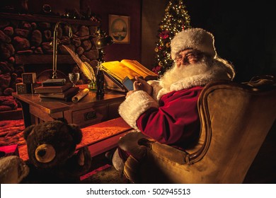 Santa Claus Using His Phone With Both Hands, Texting, While Doing His Naughty Or Nice List In His Workshop At The North Pole