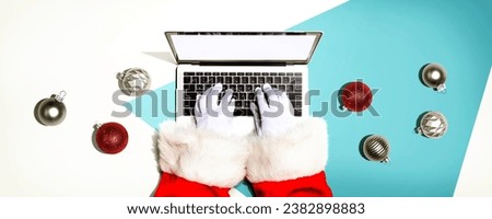 Santa Claus using a laptop computer with Christmas baubles from above
