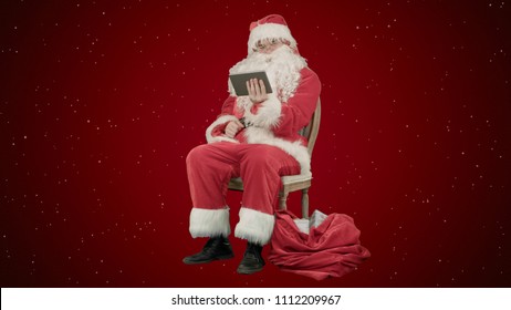 Santa Claus using tablet computer to surf internet and communicate in social media with children on red background with snow