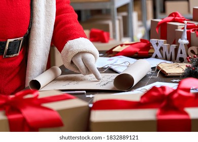 Santa Claus wearing costume reading parchment roll letter wish list standing at table with presents in workshop preparing for holiday on xmas eve. Merry Christmas wishlist background concept, closeup. - Powered by Shutterstock