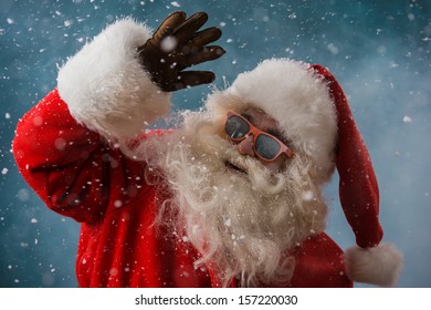 Santa Claus wearing sunglasses dancing outdoors at North Pole in snowfall. He is celebrating Christmas after hard work