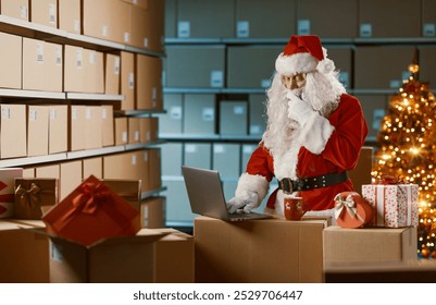 Santa Claus working with a laptop at the warehouse, he is thinking with hand on chin - Powered by Shutterstock