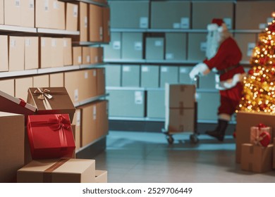 Santa Claus working in the warehouse, he is preparing delivery boxes filled with Christmas gifts - Powered by Shutterstock