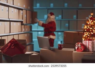 Santa Claus working in the warehouse, he is preparing delivery boxes filled with Christmas gifts - Powered by Shutterstock