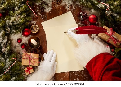 Santa Claus writing with a vintage quill pen on a sheet of blank paper surrounded by pine foliage and Christmas decorations viewed from above - Powered by Shutterstock