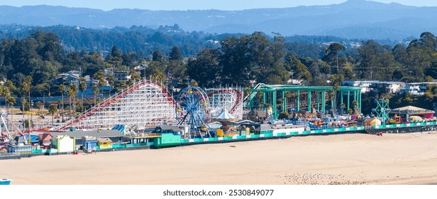 Santa Cruz Beach Boardwalk in California features rides like a wooden roller coaster and Ferris wheel, with palm trees and hills in the background. - Powered by Shutterstock