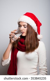 Santa Girl Drinking A Glass Of Water. Christmas Hat Isolated Portrait Of A Woman On A Gray Background.