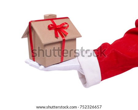Santa gives as a gift a house. A Santa's hand holds a wrapped house gift with a red ribbon. Present for the New Year. isolated on white