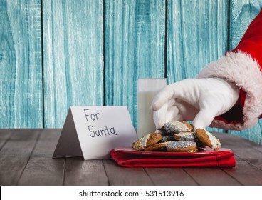 Santa Hand Holding A Cookie On Wooden Table Against Blue Background