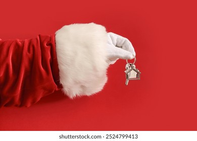 Santa hand with key and house shape keychain on red background, closeup