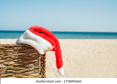 Santa hat on tropical beach.Blue sky, white sand, Egyptian or Turkish beach and sea. Winter holidays, hot sun. Wicker umbrella and deck chair. Empty beach, nobody. Without people. - Powered by Shutterstock