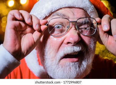 Santa Holds Broken Eyeglasses. Christmas. Santa Man With Broken Glasses. Surprised Santa Holds Broken Eye Glasses. Santa Claus Looking Through Cracked Eyeglasses.