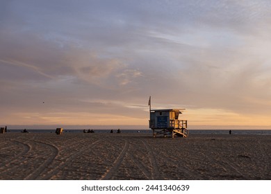 Santa Monica Beach's lifeguard tower stands watch on an empty beach, bathed in the fading light of dusk with clouds streaked across the sky. - Powered by Shutterstock
