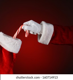 Santa Placing A Candy Cane Into A Holiday Stocking.  Square Format On A Red Background.