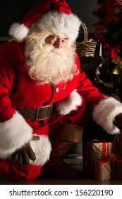 Santa Placing Gifts Under Christmas Tree In Dark Room