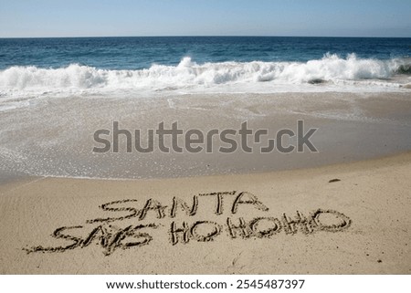 Santa says Ho Ho Ho. Santa Laughs while writing words in wet sand on a beach. The words Santa Enjoys a Beach Vacation by the ocean in the sand. Christmas Vacation. Santa Claus Enjoys the West Coast.