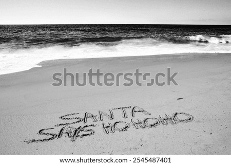 Santa says Ho Ho Ho. Santa Laughs while writing words in wet sand on a beach. The words Santa Enjoys a Beach Vacation by the ocean in the sand. Christmas Vacation. Santa Claus Enjoys the West Coast.