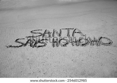 Santa says Ho Ho Ho. Santa Laughs while writing words in wet sand on a beach. The words Santa Enjoys a Beach Vacation by the ocean in the sand. Christmas Vacation. Santa Claus Enjoys the West Coast.