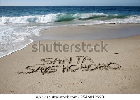 Santa says Ho Ho Ho. Santa Laughs while writing words in wet sand on a beach. The words Santa Enjoys a Beach Vacation by the ocean in the sand. Christmas Vacation. Santa Claus Enjoys the West Coast.