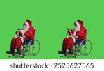 Santa texting and being on videocall dealing with chronic impairment, using smartphone against full body greenscreen. Young man saint nick talks on online teleconference meeting.