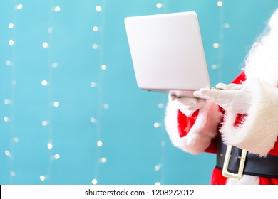 Santa using a laptop on a shiny light blue background - Shutterstock ID 1208272012