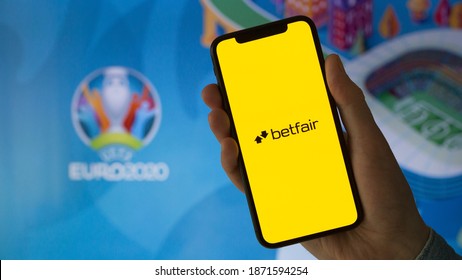 Santa Venera, Malta - December 08 2020: A man holds a phone with Betfair logo in his hand next to the TV. Euro 2020 betting at Betfair.