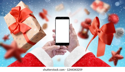 Santa's Hands Holding Black Phone With Isolated Screen On Blue Background Surrounded With Gift Box, Red Ribbon And Xmas Tree Ornaments. Mockup