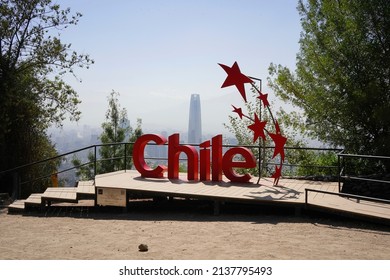 Santiago - Chile - March 05, 2022 - red sign reading "Chile" and red stars at the top of San Cristobald park and hill with Costanera center tower on the background  during sunny foggy morning.