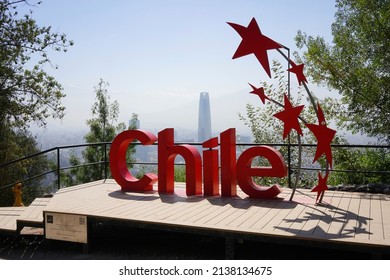 Santiago - Chile - March 05, 2022 - Red sign reading "Chile" and red stars along the road going up San Cristobal park hill with Costanera center tower in the background. 