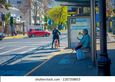 SANTIAGO, CHILE - SEPTEMBER 13, 2018: Unidentified Woman Waiting The Bus In A Busstop With Some People Riding A Bike In Downtown Street Of The City Of Santiago