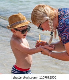 Santiago De La Ribera, Murcia / Spain - June 10 2018: Mum Writes Her Phone Number On Her Son's Arm In Case He Gets Lost On The Beach. Lady With Blond Plaits, Little Boy With Hat.