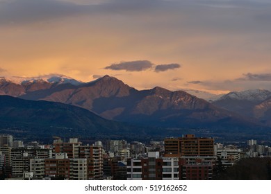 Santiago mountain range at sunset with city buildings in the shade and colored sky.