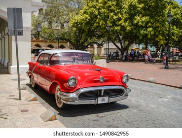 SANTO DOMINGO/DOMINICAN REPUBLIC - APRIL 20, 2019: Red old classic american car parked in front of Parque Colon at colonial zone in Santo Domingo.