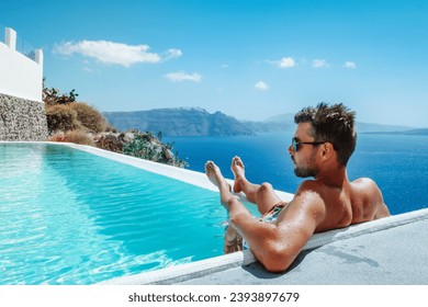 Santorini Greece Oia, young men in swim short relaxing in the pool looking out over the caldera of Santorini Island Greece, infinity pool, a young guy on a luxury vacation in Europe Greece. 