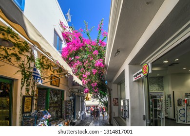 Santorini, Greece - September 16 2018: A colorful, narrow street with souvenir shops and pink bloomed bougainvillea flowers overhead, in the tourist center of Santorini Greece.