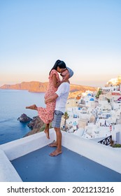 Santorini Greece, Young Couple Mid Age European And Asian On Vacation At The Greek Village Of Oia Santorini Greece, Luxury Vacation Santorini. Mid Age Man And Woman Watching Sunset Santorini