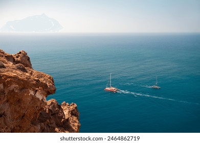 Santorini island, Greece. Yachts sailing near the sea coast. Clear blue sea and red volcanic rocks. Summer seascape.  - Powered by Shutterstock