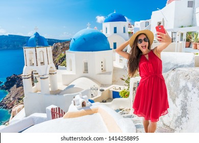 Santorini tourist girl on cruise holiday taking selfie photo with phone at famous three domes church, European tourism attraction in Greece. Asian woman on vacation.