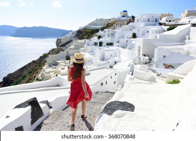 Santorini travel tourist woman on vacation in Oia walking on stairs. Person in red dress visiting the famous white village with the mediterranean sea and blue domes. Europe summer destination