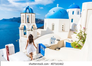 Santorini travel tourist woman on vacation in Oia walking on stairs. Person in white dress visiting the famous white village with the mediterranean sea and blue domes. Europe summer destination.