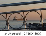 Santos city, Brazil. Water channel nº6 on the beach during sunset. Cargo ship on the horizon. In the foreground the handrail railing of the bridge over the water channel. 