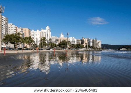 Santos city, Brazil. Waterfront buildings reflected in the sea water of the beach during high tide in the neighborhood of Ponta da Praia. In the background, the fortress of Barra.