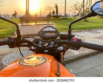 Santos, São Paulo - Brazil - August 20, 2021: Front partial view of an orange motorcycle brand Kawasaki, model Er6n. Stop in the Ponta da Praia region at sunset.