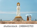 Sanya, China: Tourist with an umbrella takes pictures girl near a giant statue the Guan Yin of the South Sea in Nanshan temple