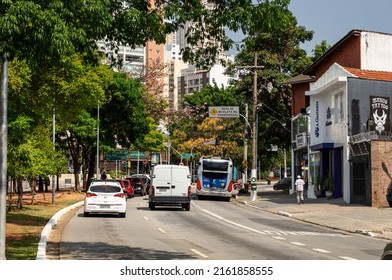SAO PAULO - BRAZIL - SEP 27, 2021: Cars passing by a curved section of Sumare avenue in Perdizes district area nearby small local shops in a normal business day under sunny clear blue sky.