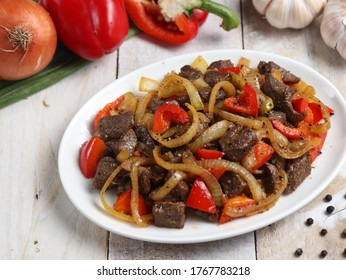 Sapi lada hitam, Indonesian and Chinese cuisine, stir fried beef with black pepper sauce and red bell peppers in white plate on wooden table.