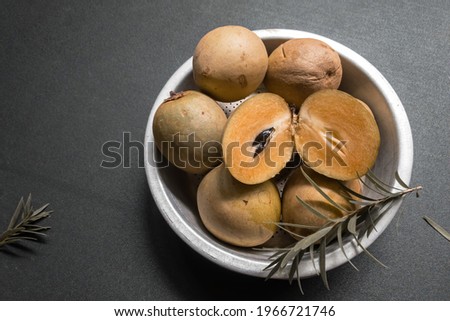 Sapodilla slices in zinc bowl  with green leaves on black background